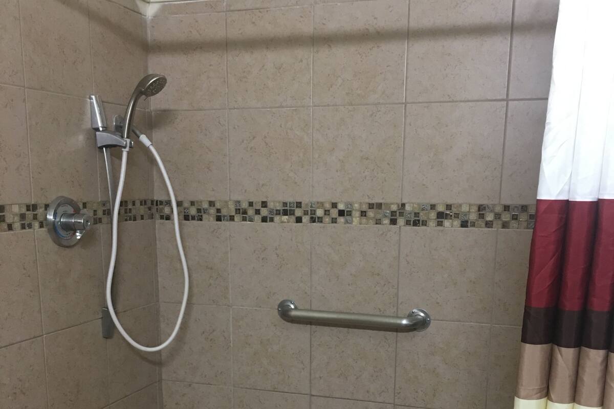 A shower area with a handrail, tiled walls, and a drain on the floor.