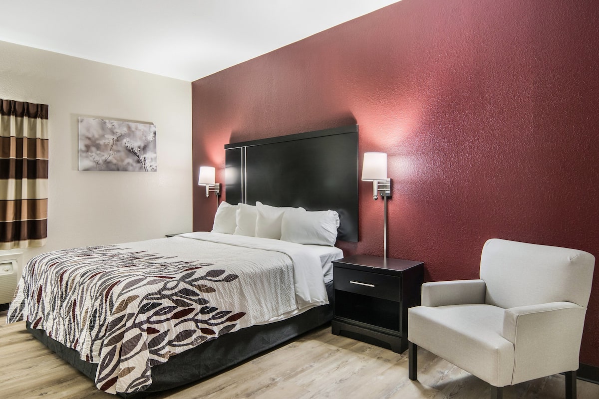 A hotel room with a bed, bedside lamps, a chair, and a painting on the wall.