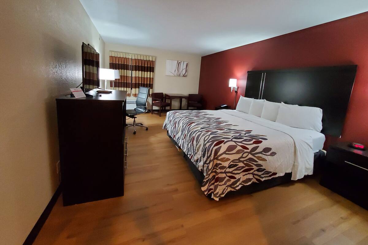 A hotel room with a bed, desk, chair, and a desk lamp.