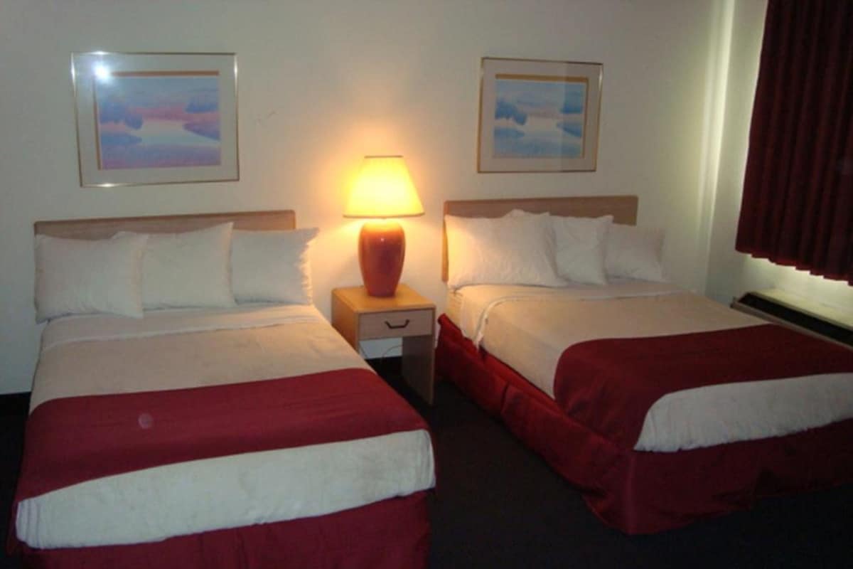 A hotel room with two beds, each with a red and white bedspread, a nightstand with a lamp, and two framed pictures on the wall.