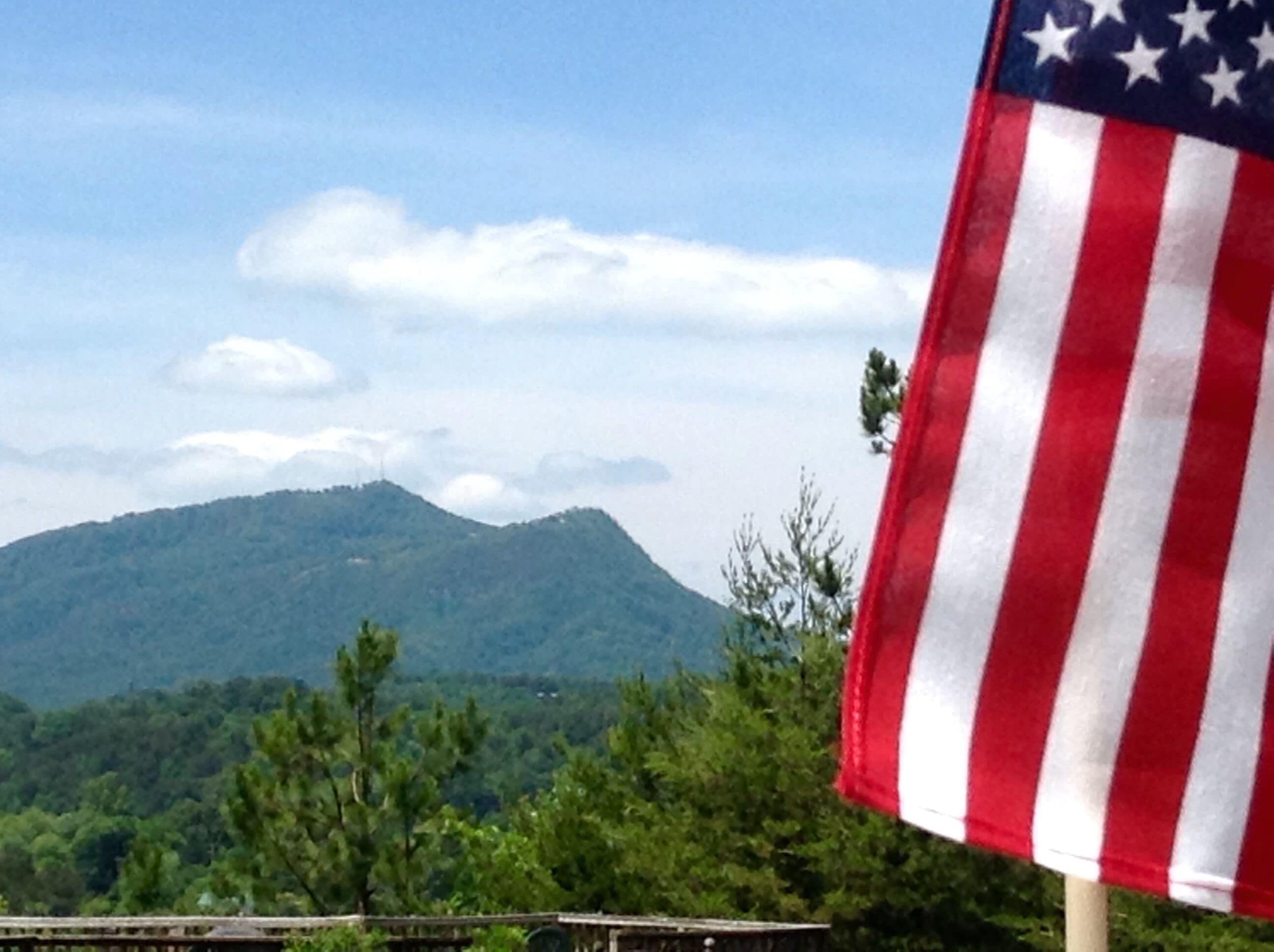 An American flag on a flagpole with a mountainous landscape in the background.