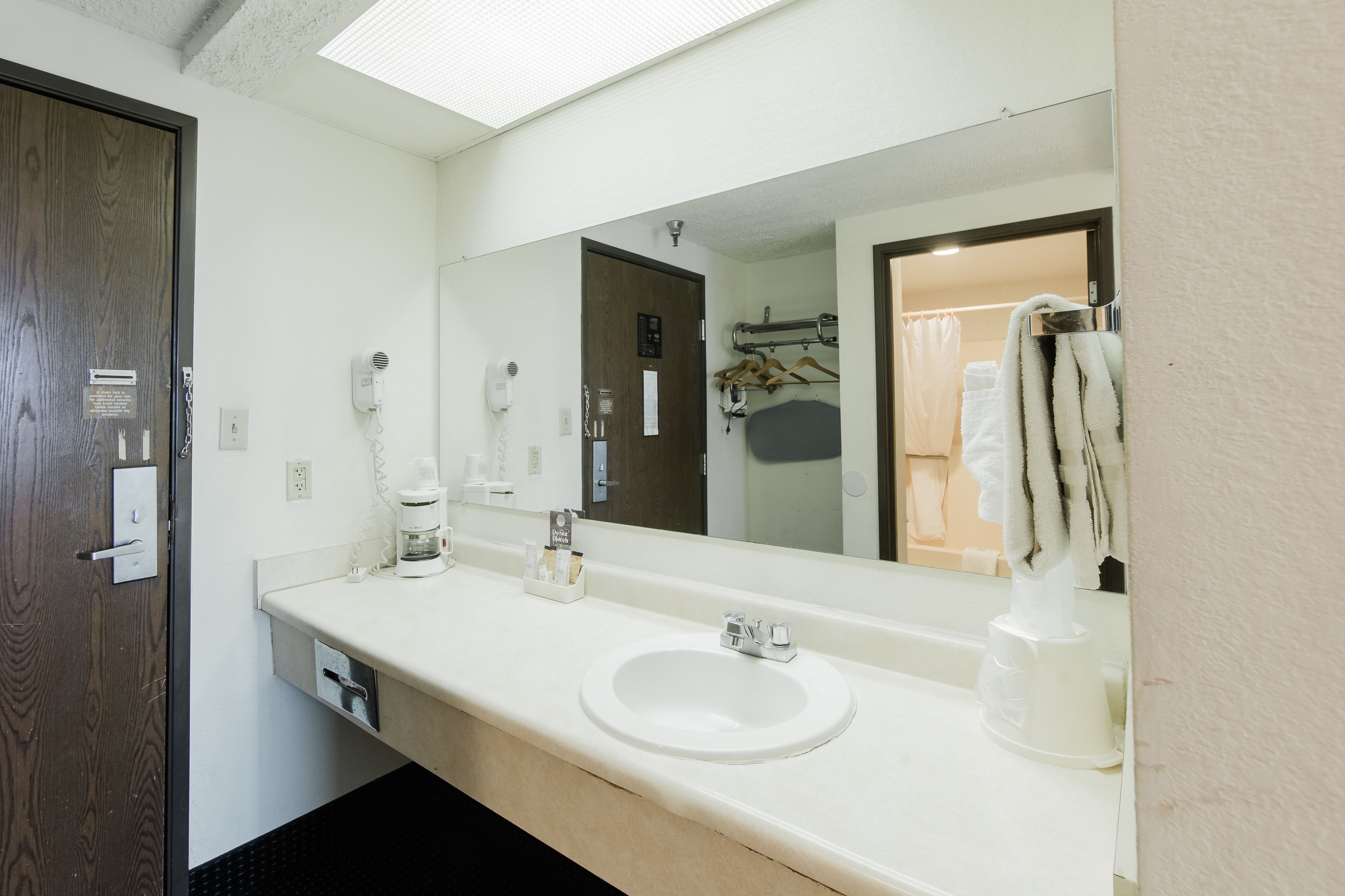 Une salle de bain d’hôtel avec un lavabo blanc, un grand miroir, un sèche-cheveux et un porte-serviettes.