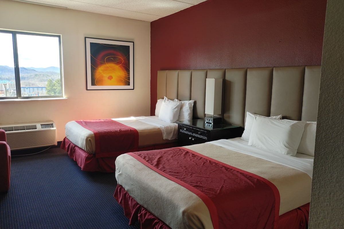 A hotel room with two beds, a large window, an air conditioning unit, and a painting on the wall.