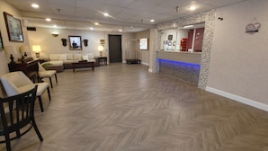 A hotel lobby with a reception desk, seating area with sofas and chairs, and a herringbone patterned floor.