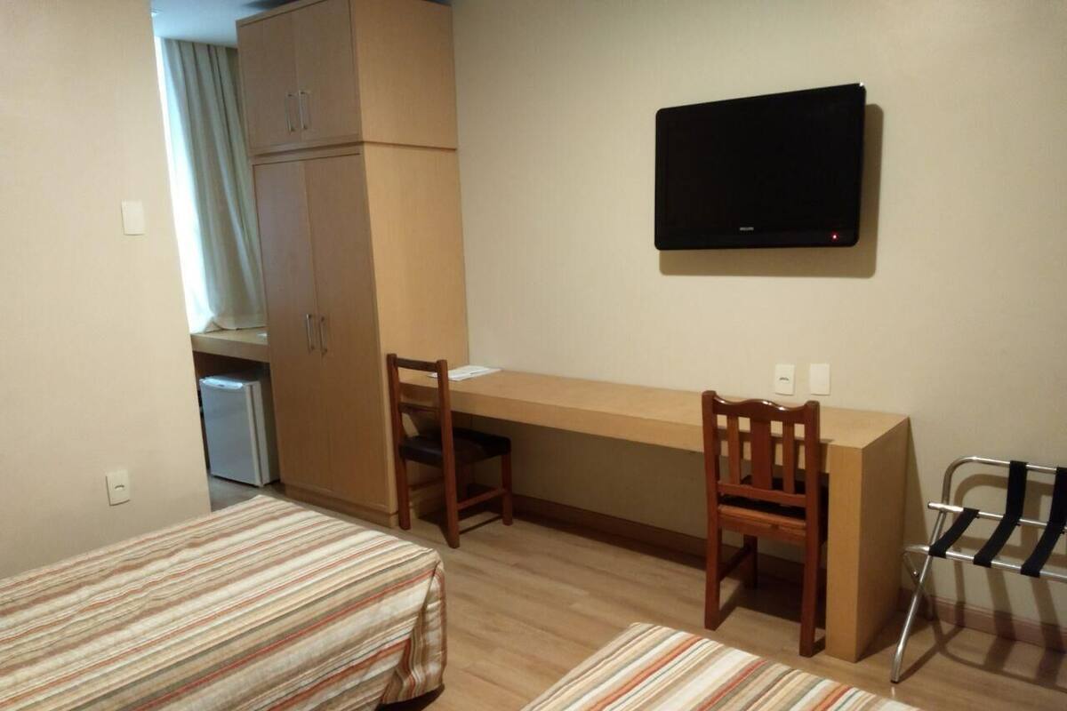 Ein kleiner, ordentlicher Raum mit einem Bett, einem Schreibtisch und einem Fernseher.