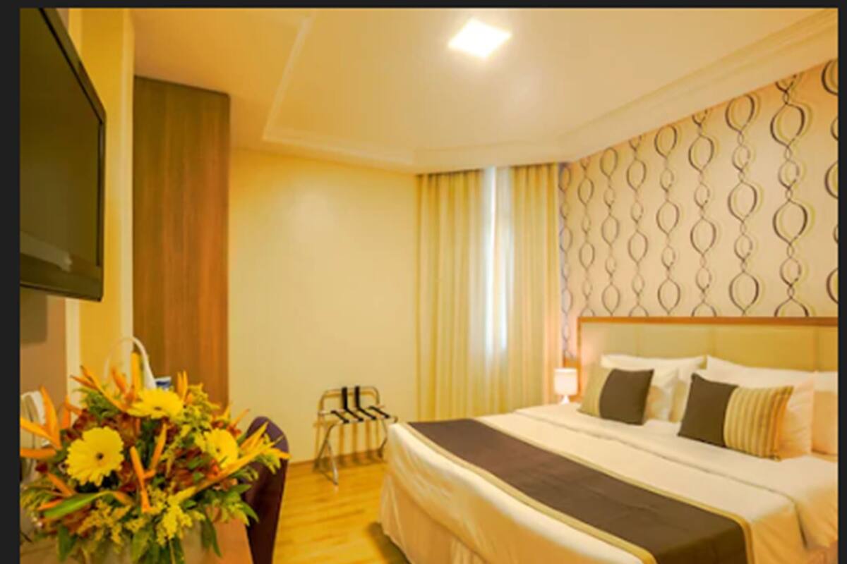 Ein Hotelzimmer mit einem Bett, einem Schreibtisch mit Stuhl, einer Blumenvase und einer Wand mit geometrischem Muster.