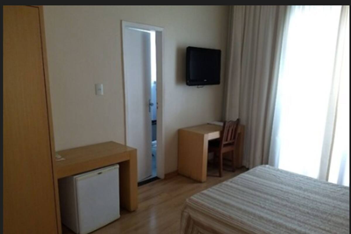 Ein Hotelzimmer mit Bett, Schreibtisch, Stuhl, Fernseher und kleinem Kühlschrank.