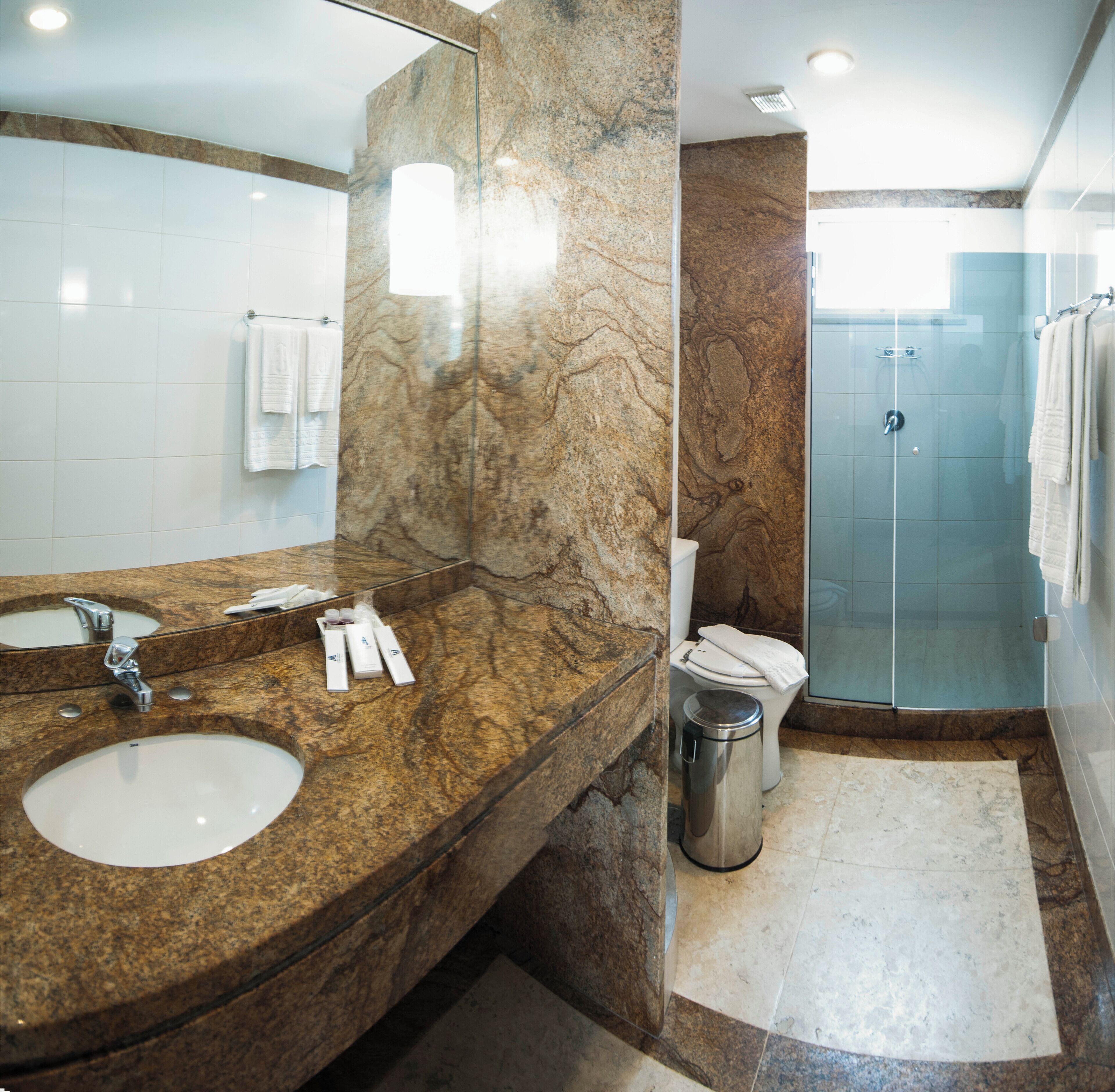 A bathroom with a marble vanity, a sink, a toilet, and a glass shower enclosure.