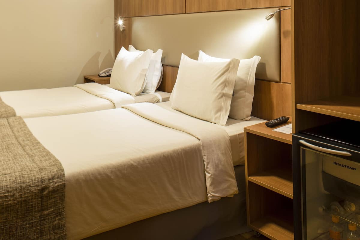 Habitación de hotel con cama, mesitas de noche, minibar y aire acondicionado instalado en la pared.