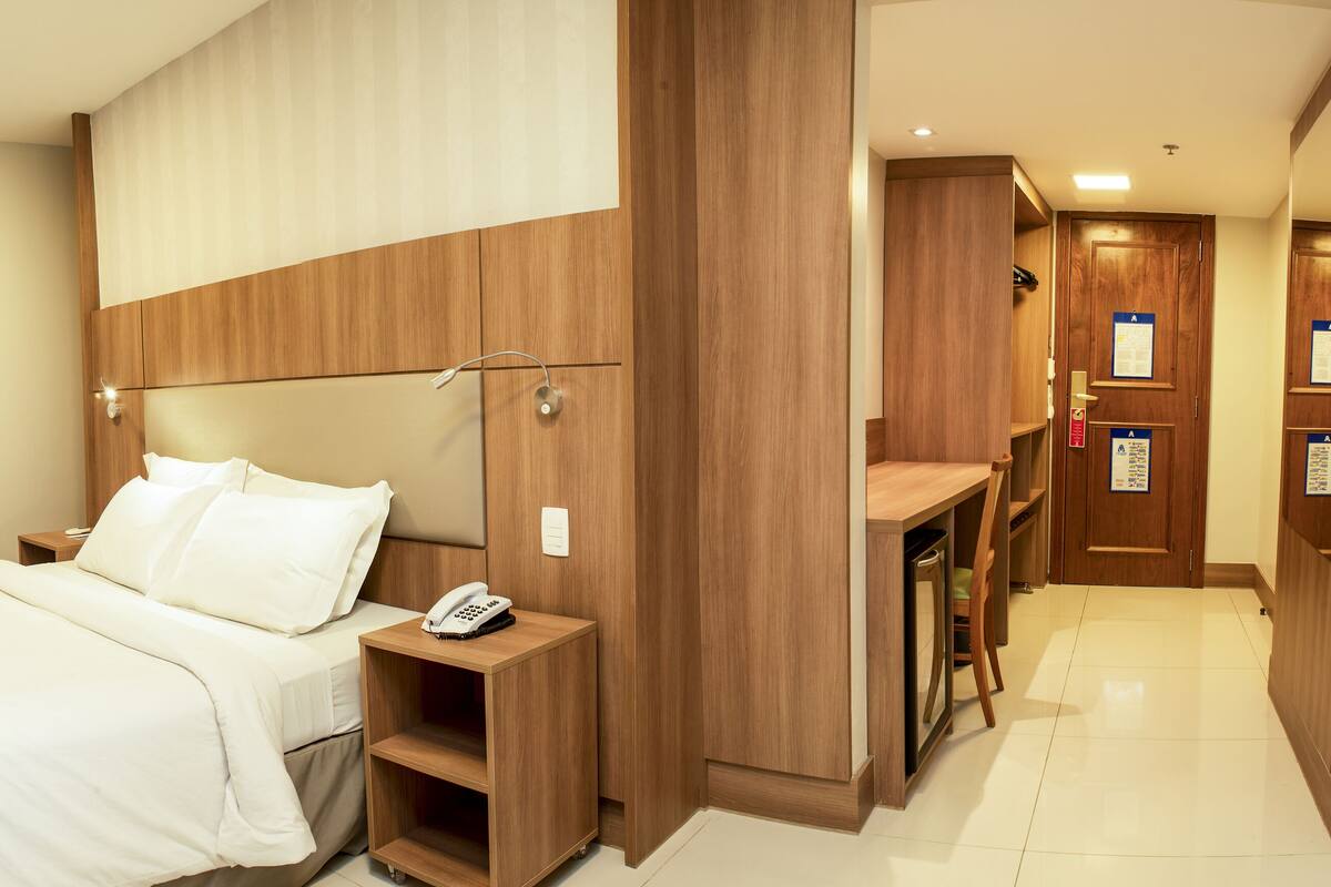 Una habitación de hotel con cama, mesita de noche y televisor montado en la pared.