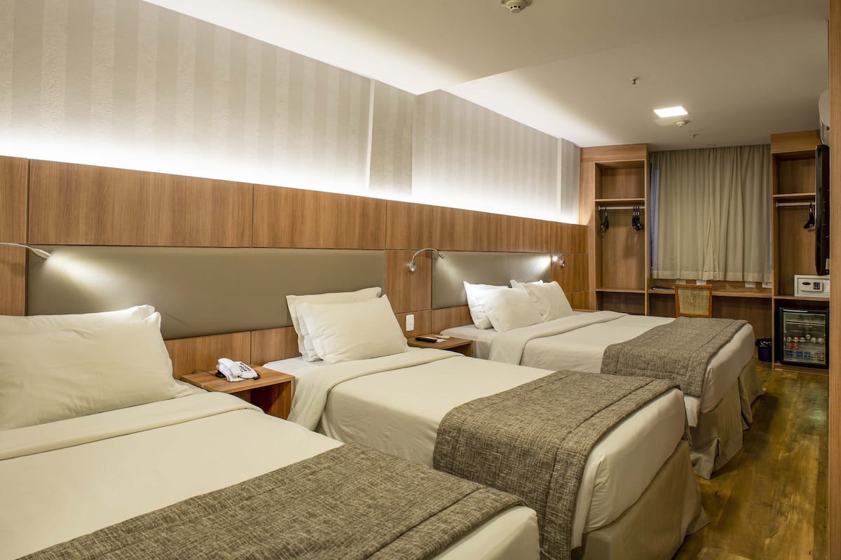 Habitación de hotel con tres camas, un armario, un minibar y zona de ducha.