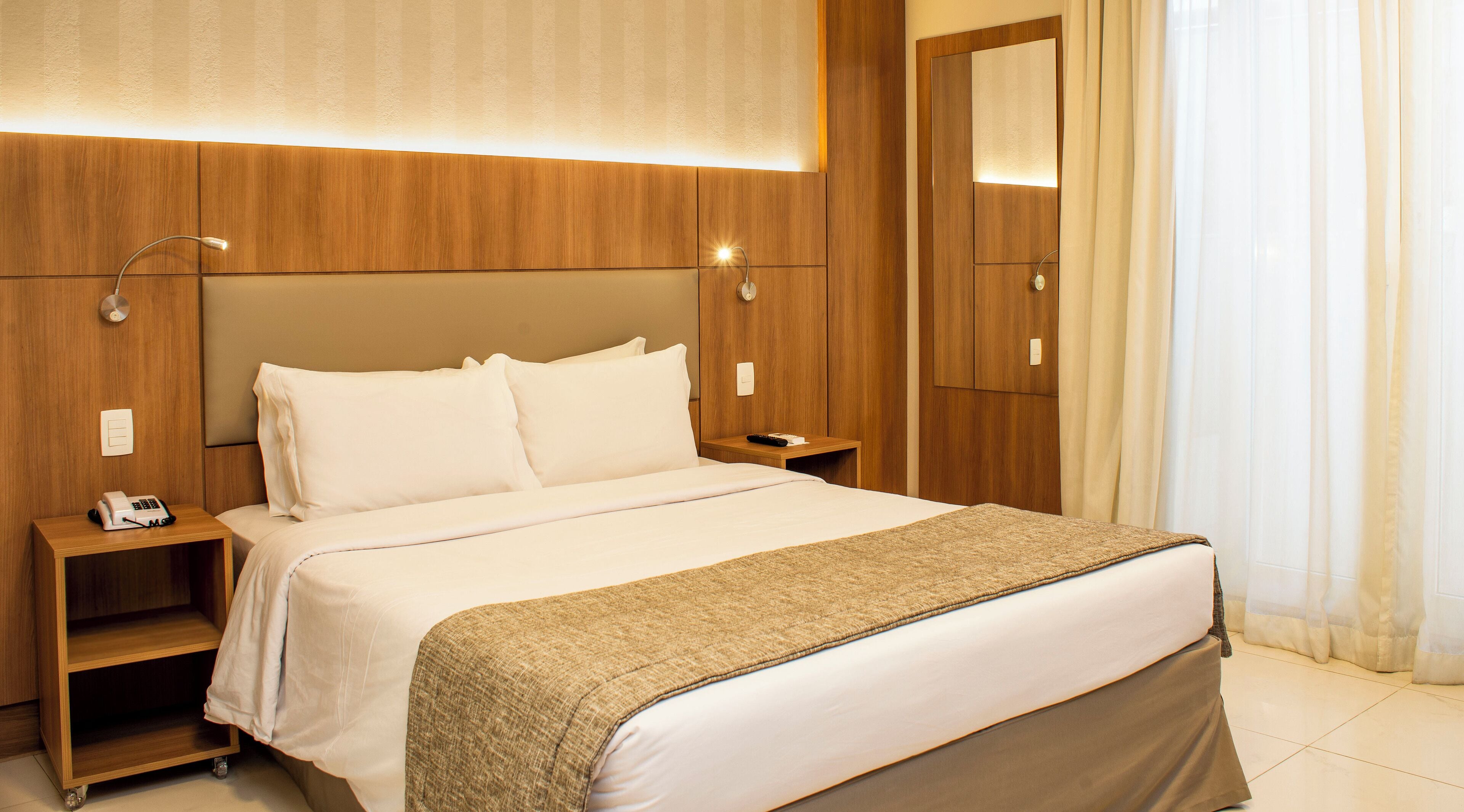 Ein Hotelzimmer mit einem großen Bett, einem Holzkopfstück, Nachttischen mit Lampen und einem Spiegel.