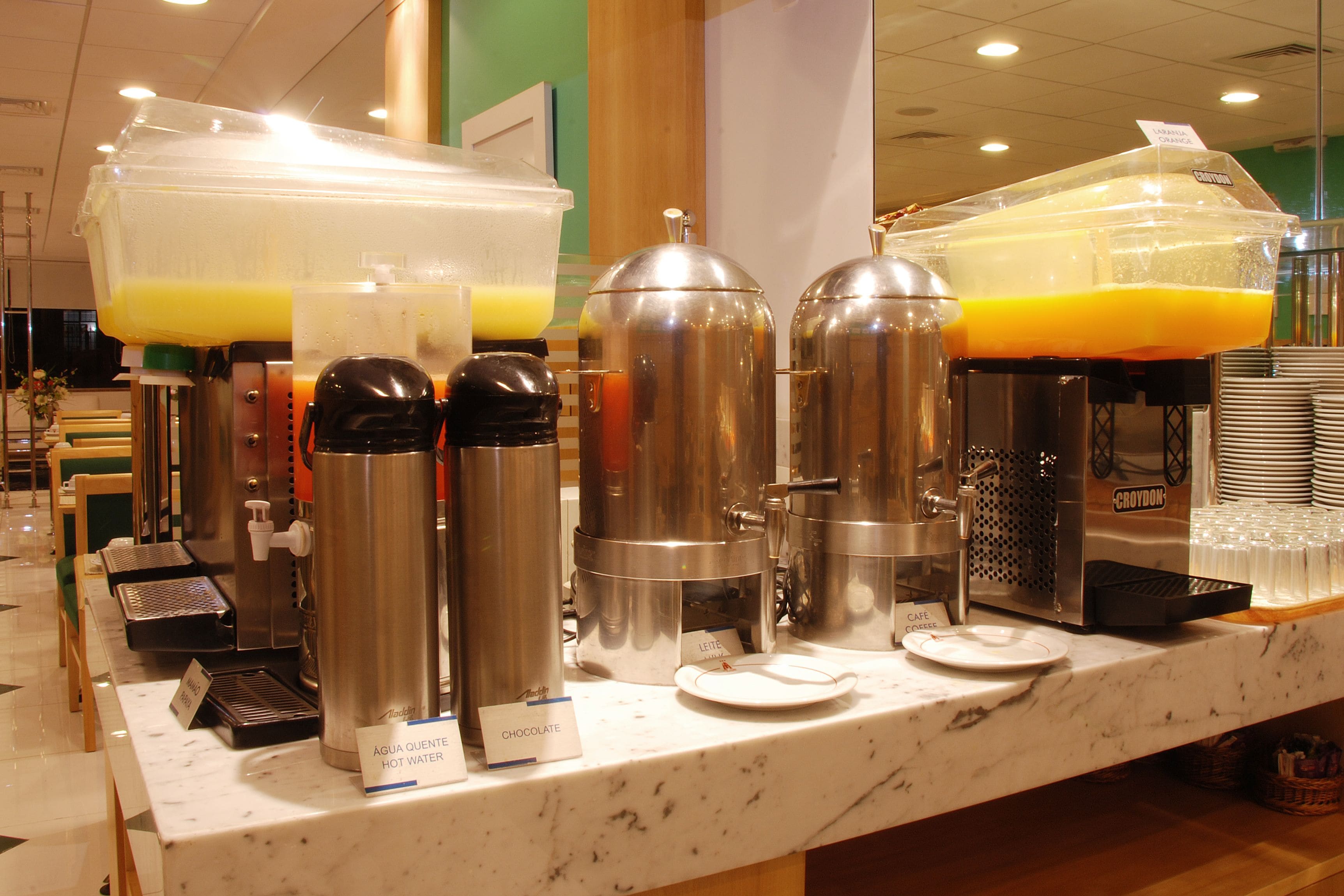 A breakfast bar with multiple beverage dispensers, including hot water and orange juice, and a coffee machine.