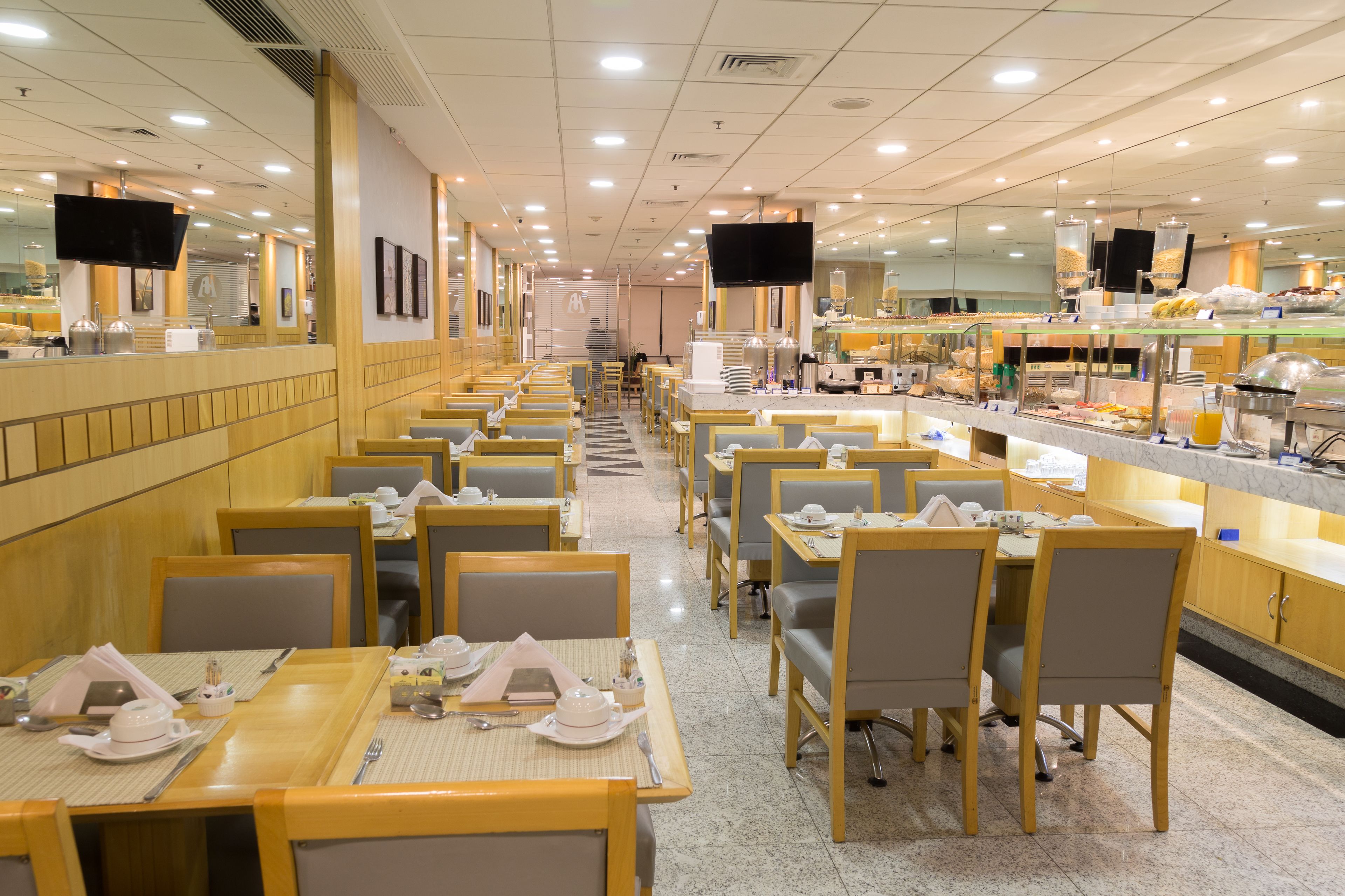 A spacious dining area with multiple tables and chairs, a buffet counter, and a television mounted on the wall.