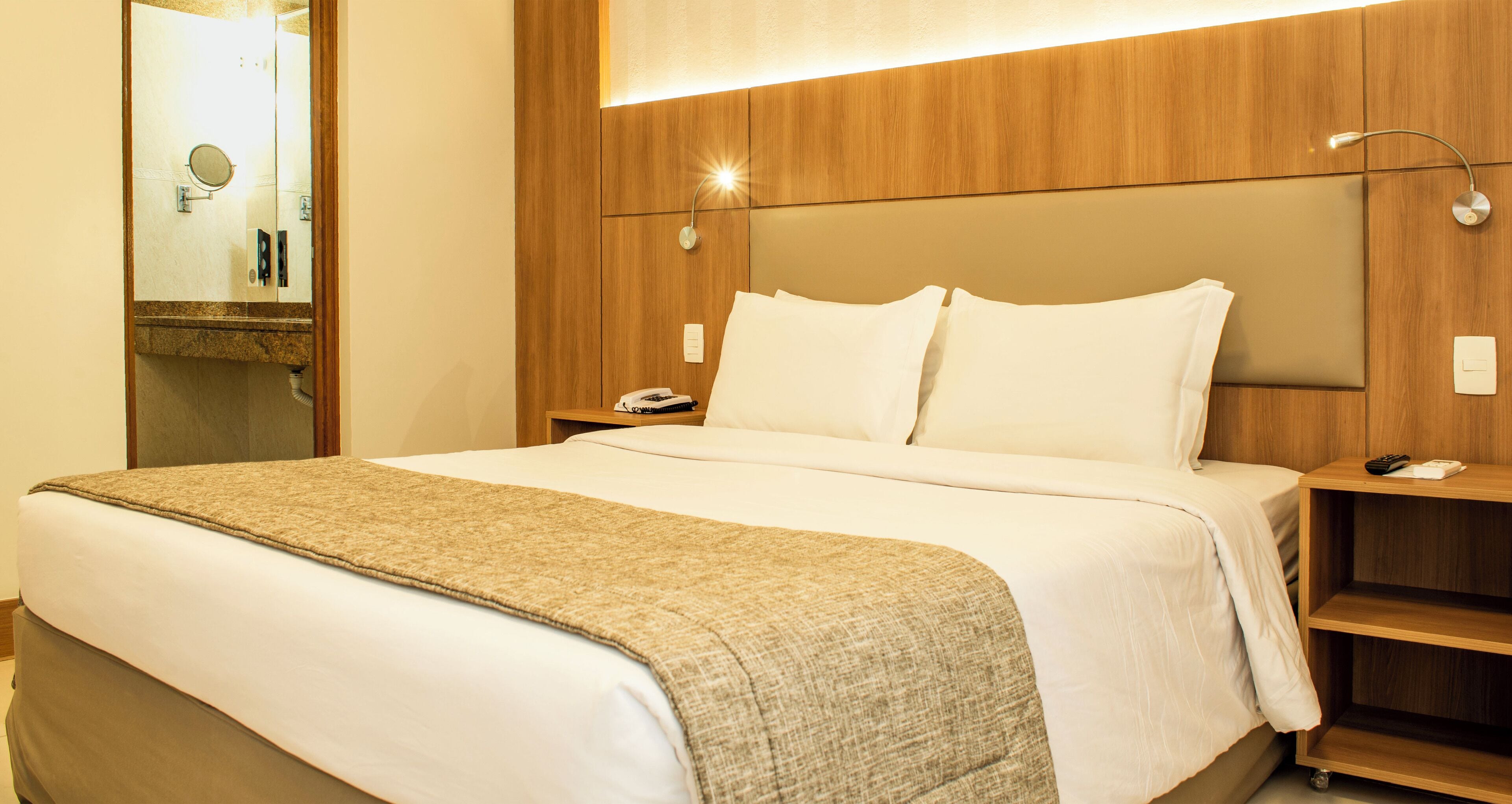 A hotel room with a large bed, a wooden headboard, a bedside table with a phone, and a nightstand with a lamp.