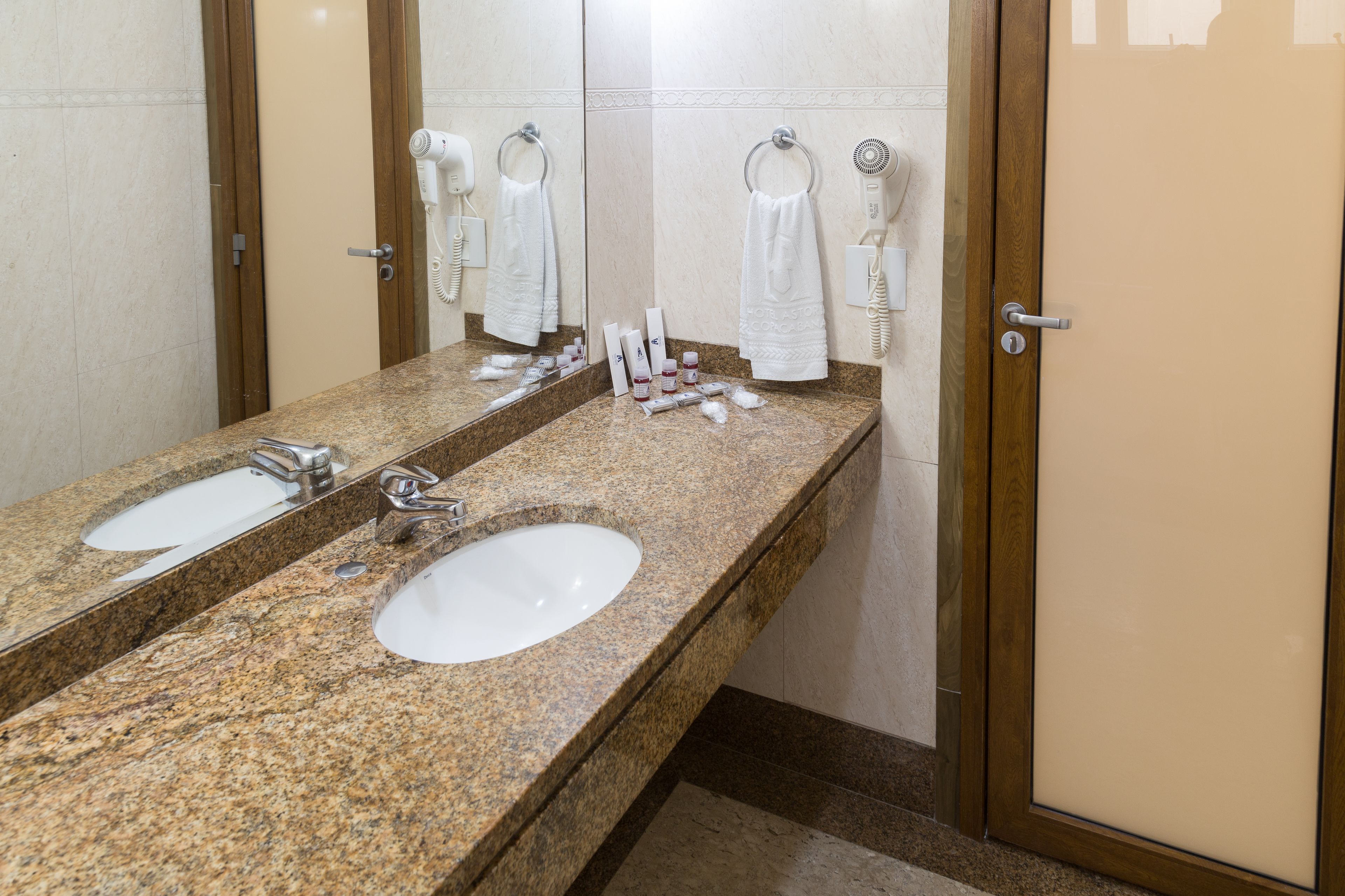 A bathroom with a granite countertop, two sinks, a large mirror, and a towel rack.