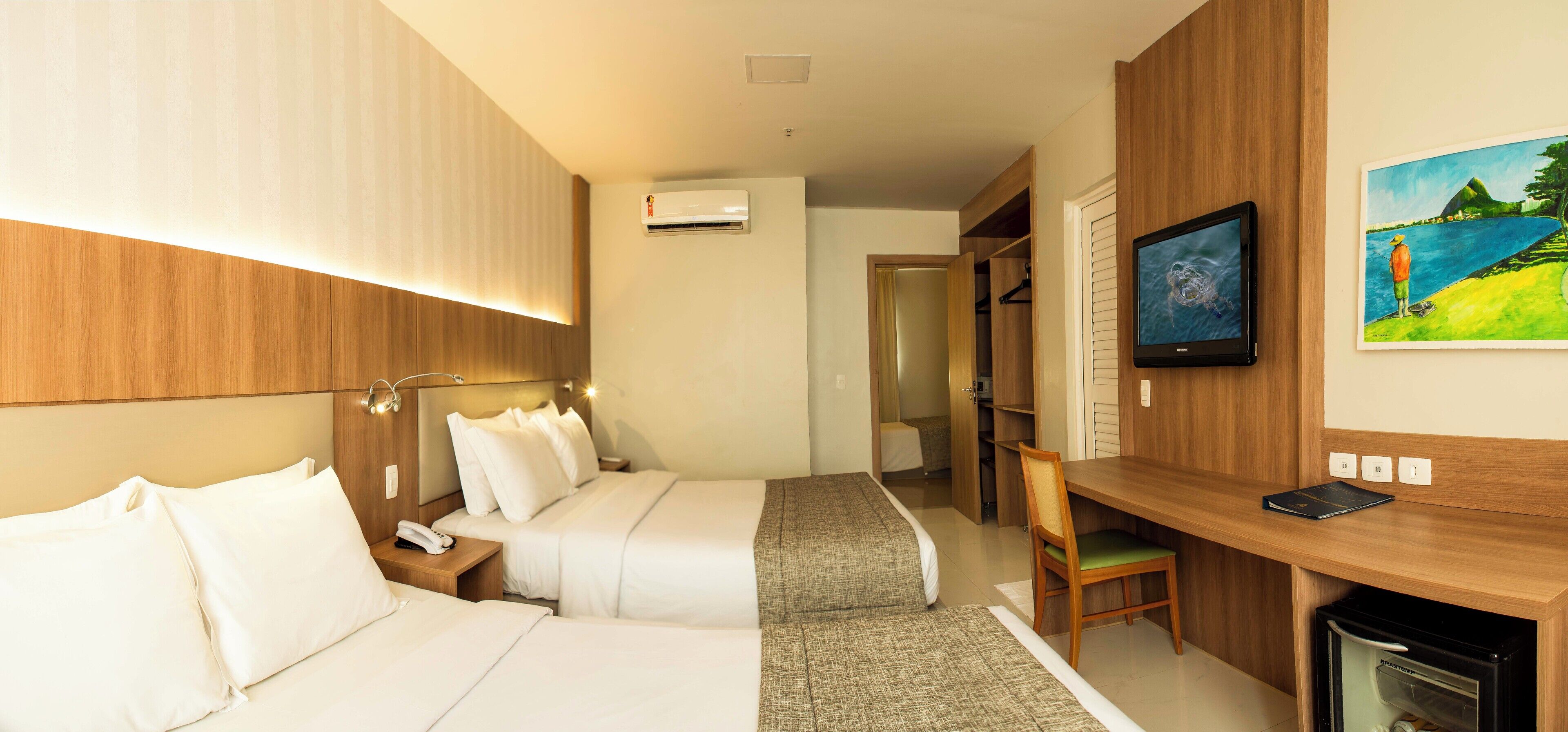 Ein Hotelzimmer mit zwei Betten, einem Schreibtisch, einem Fernseher und einem Gemälde.