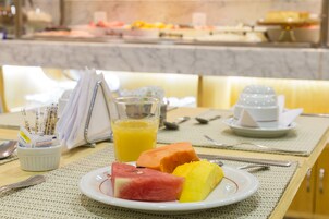 A breakfast setting with a plate of fruit, a glass of orange juice, and a cup of coffee on a table.