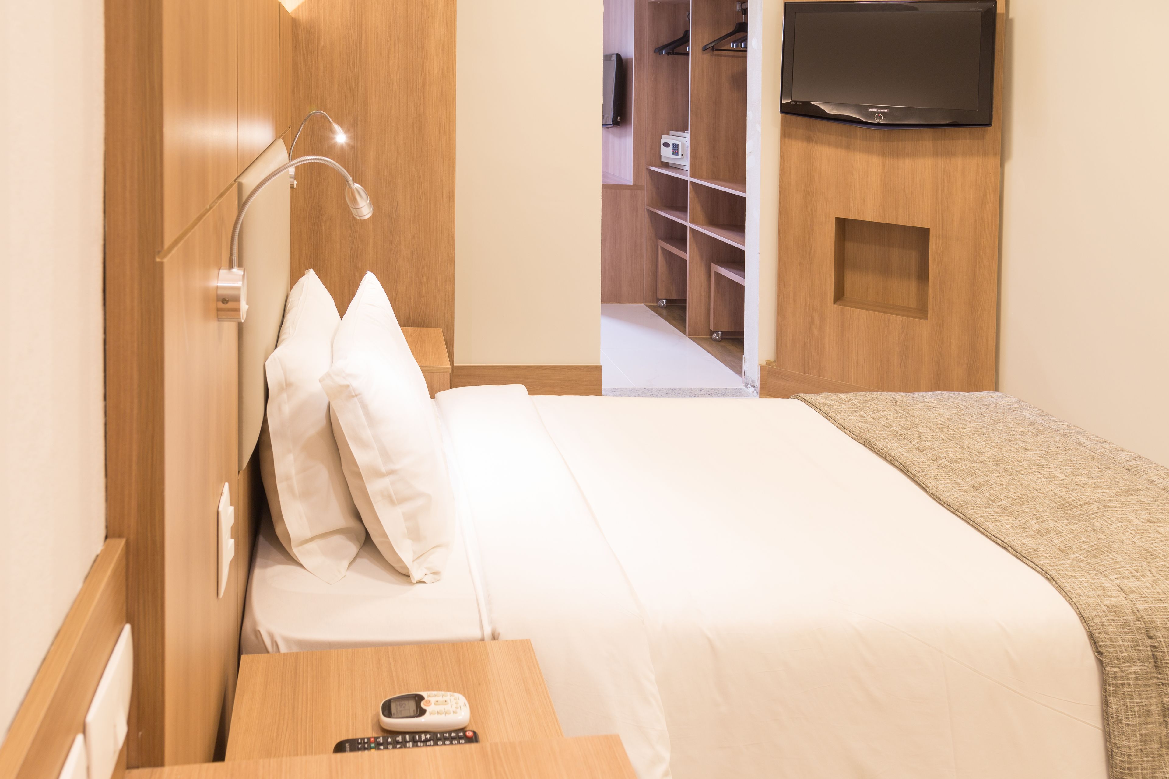 A hotel room with a bed, bedside table, lamp, and a TV mounted on the wall.
