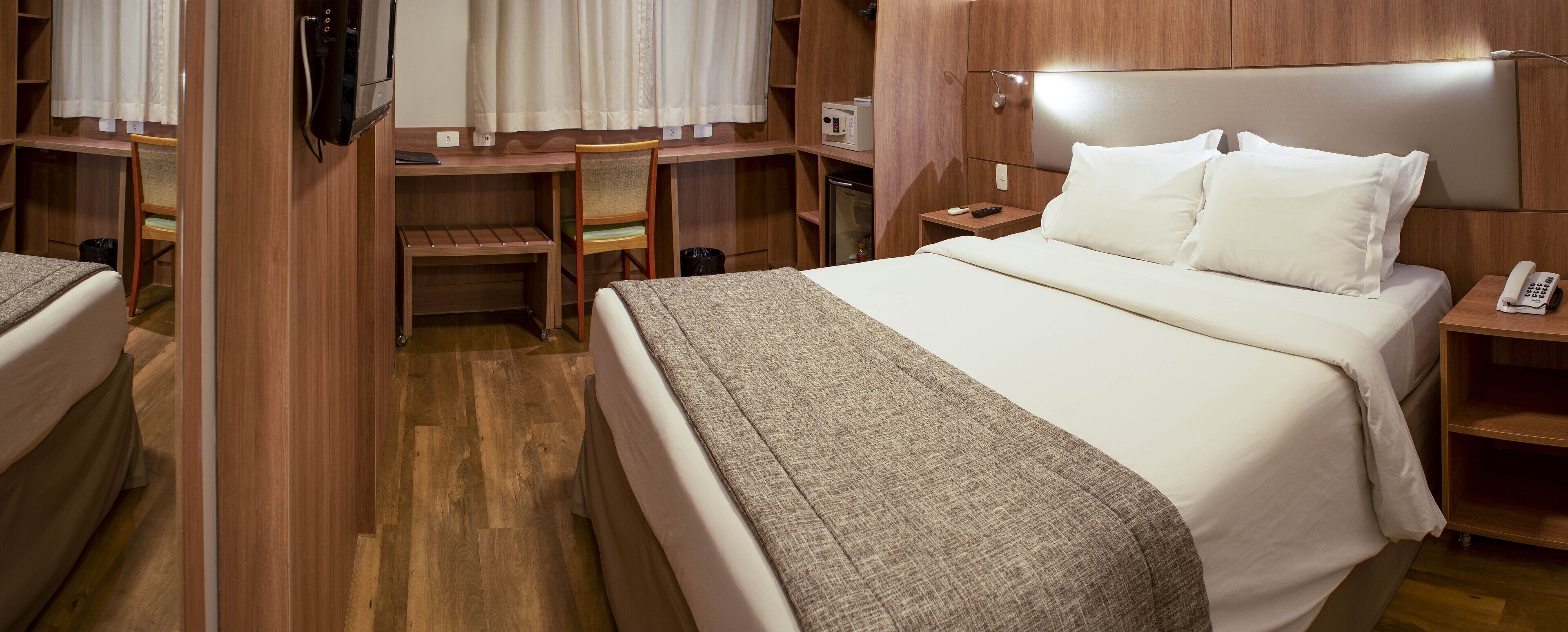 A compact hotel room with a single bed, a desk, a chair, and a small kitchenette.