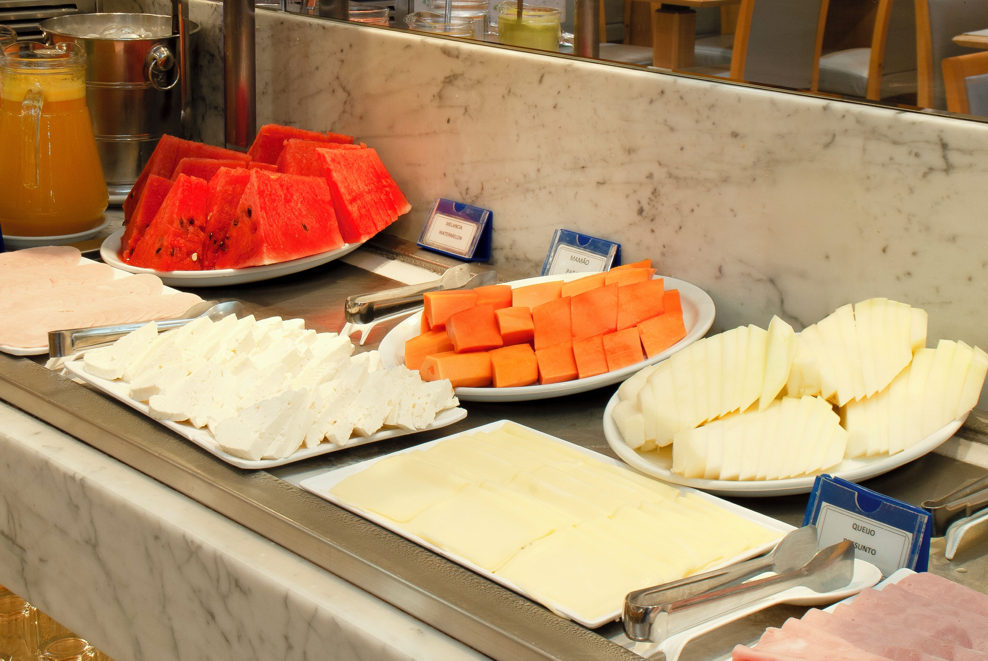 Un buffet proposant une variété de plats, notamment des pastèques, des fromages et d’autres plats préparés.