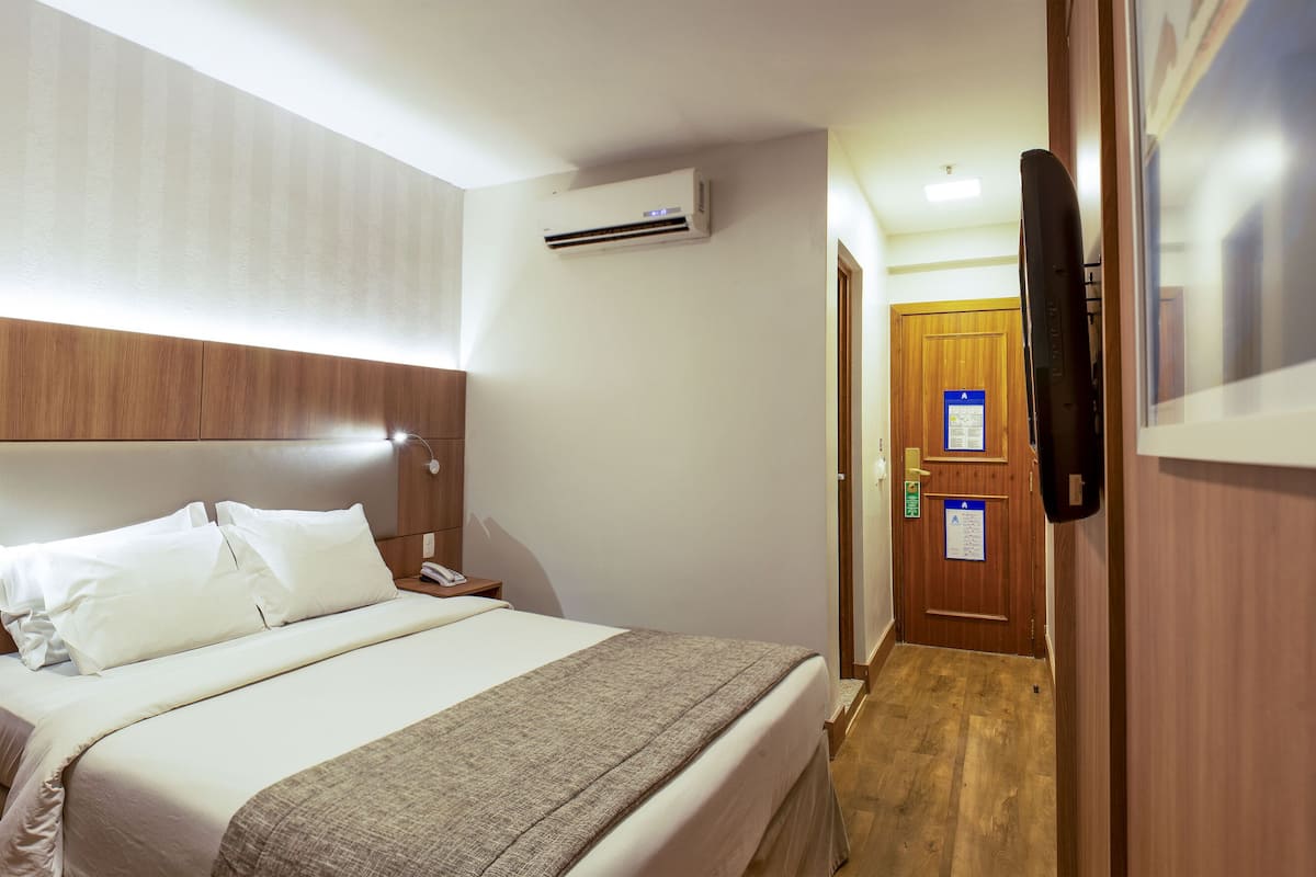 Una habitación de hotel con cama, mesita de noche y televisión.