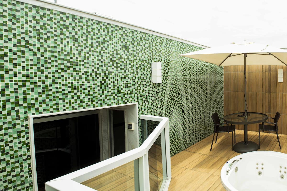 Una terraza en la azotea con un muro cubierto de mosaicos, un muro de paneles de madera, un jacuzzi con cerramiento de vidrio, una mesa redonda con sillas y una planta en maceta.
