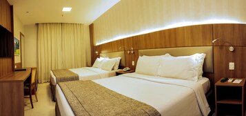 A hotel room with two beds, a desk, a chair, a nightstand, and a wall-mounted TV.