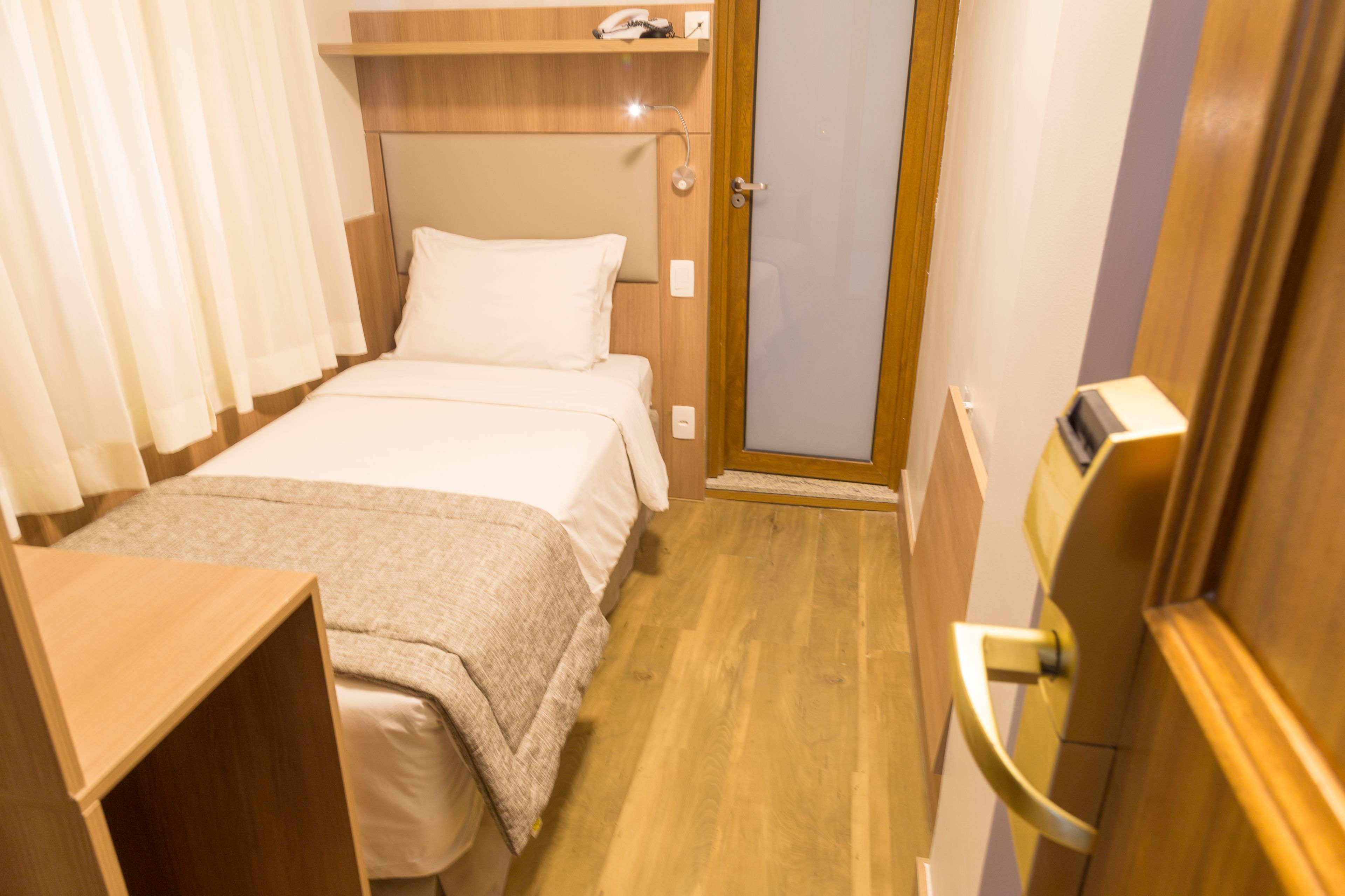 Un dormitorio pequeño y ordenado con cama, mesita de noche y una puerta que da a otra habitación.