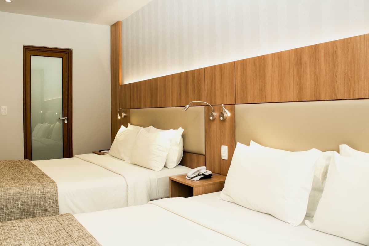 Habitación de hotel con dos camas, cabecero de madera, mesita de noche con teléfono y espejo.