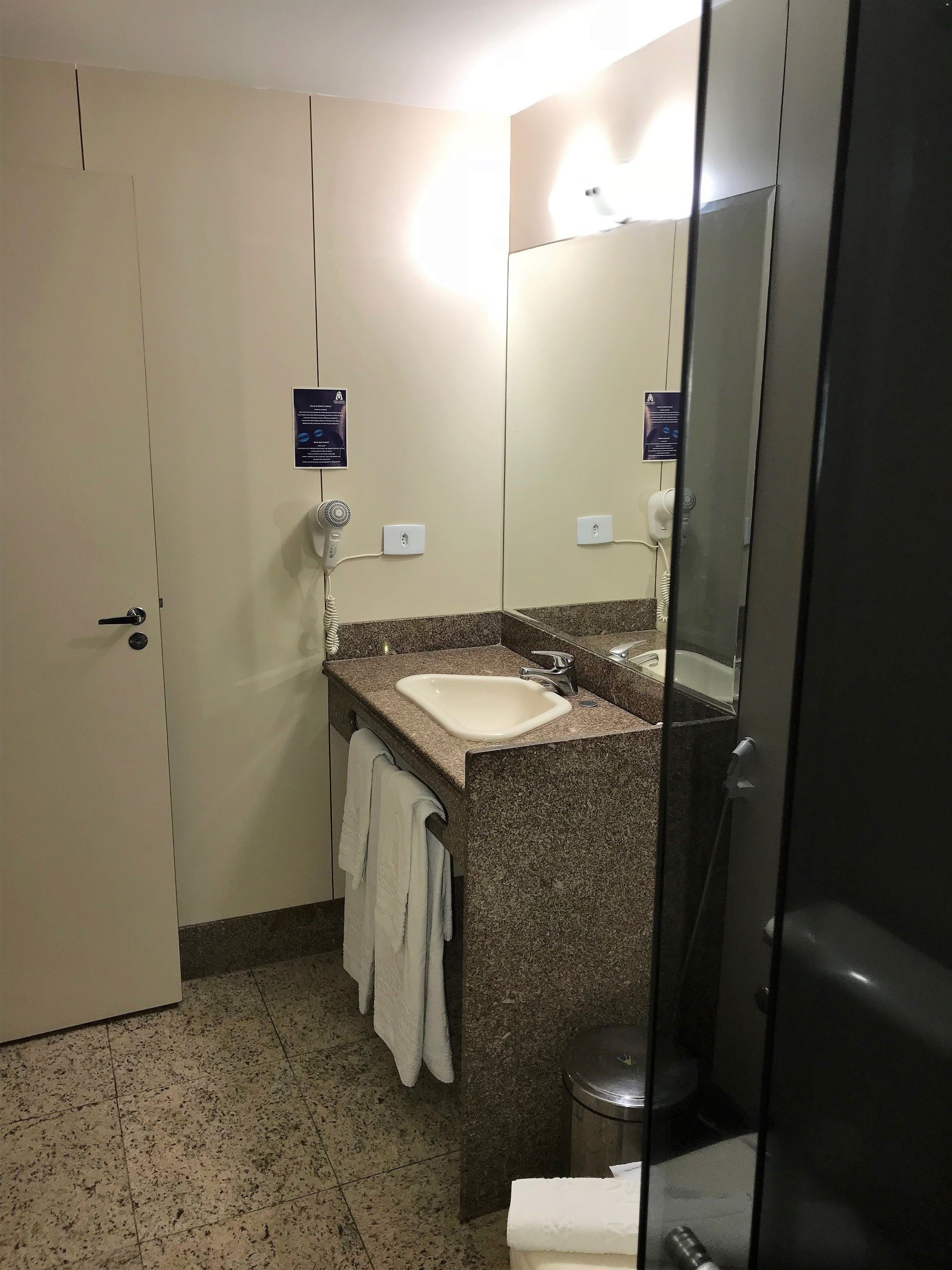 Casa de banho com lavatório, espelho, porta-toalhas e um cesto de lixo.