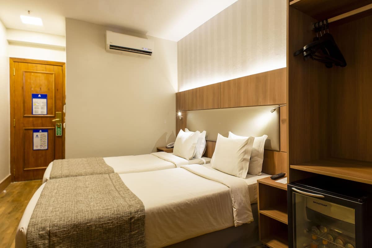 Habitación de hotel con dos camas, minibar, televisión y paneles de madera en las paredes.