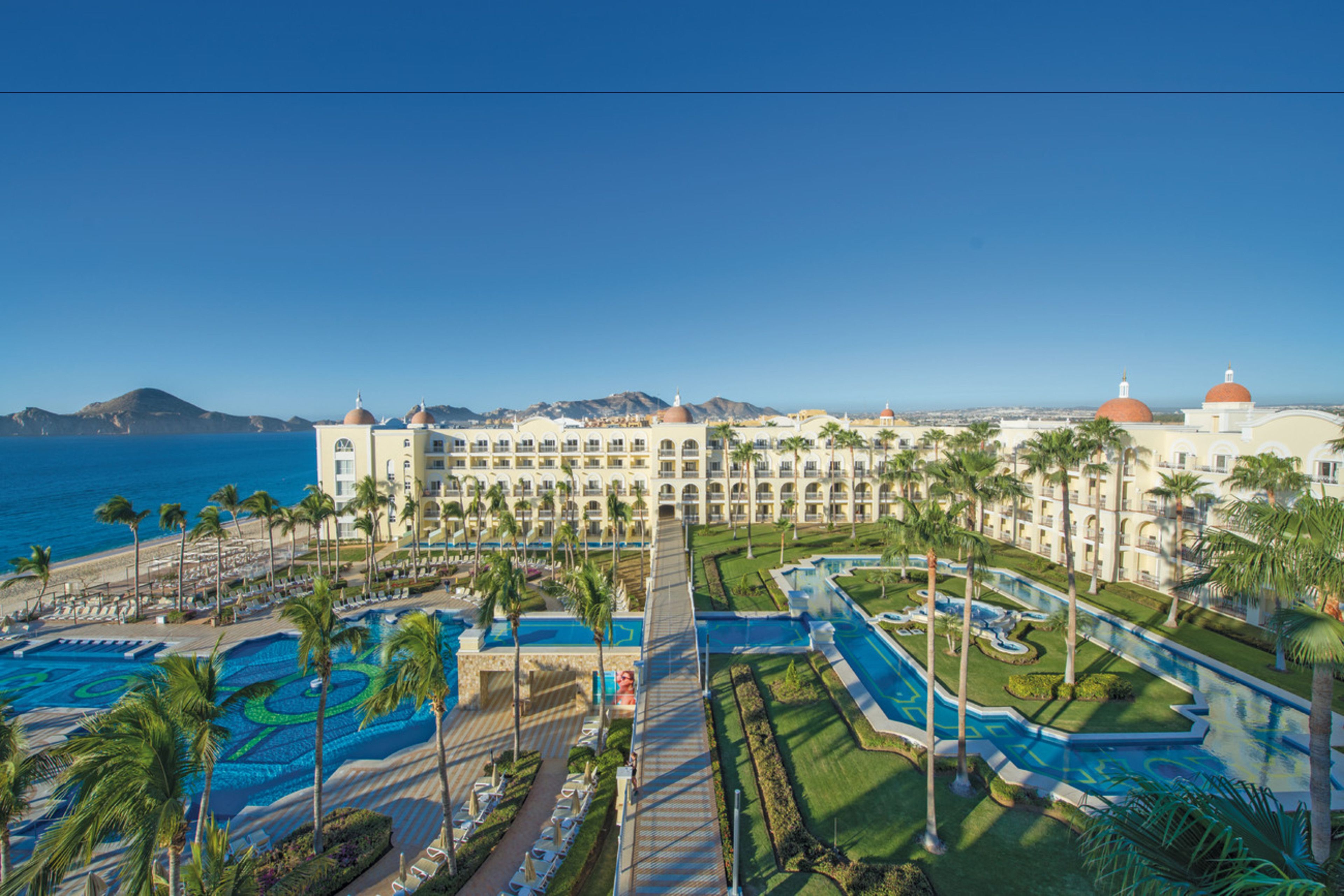 Un hotel con un amplio área de piscina, palmeras y vista al océano.