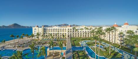Un hotel con un amplio área de piscina, palmeras y vista al océano.