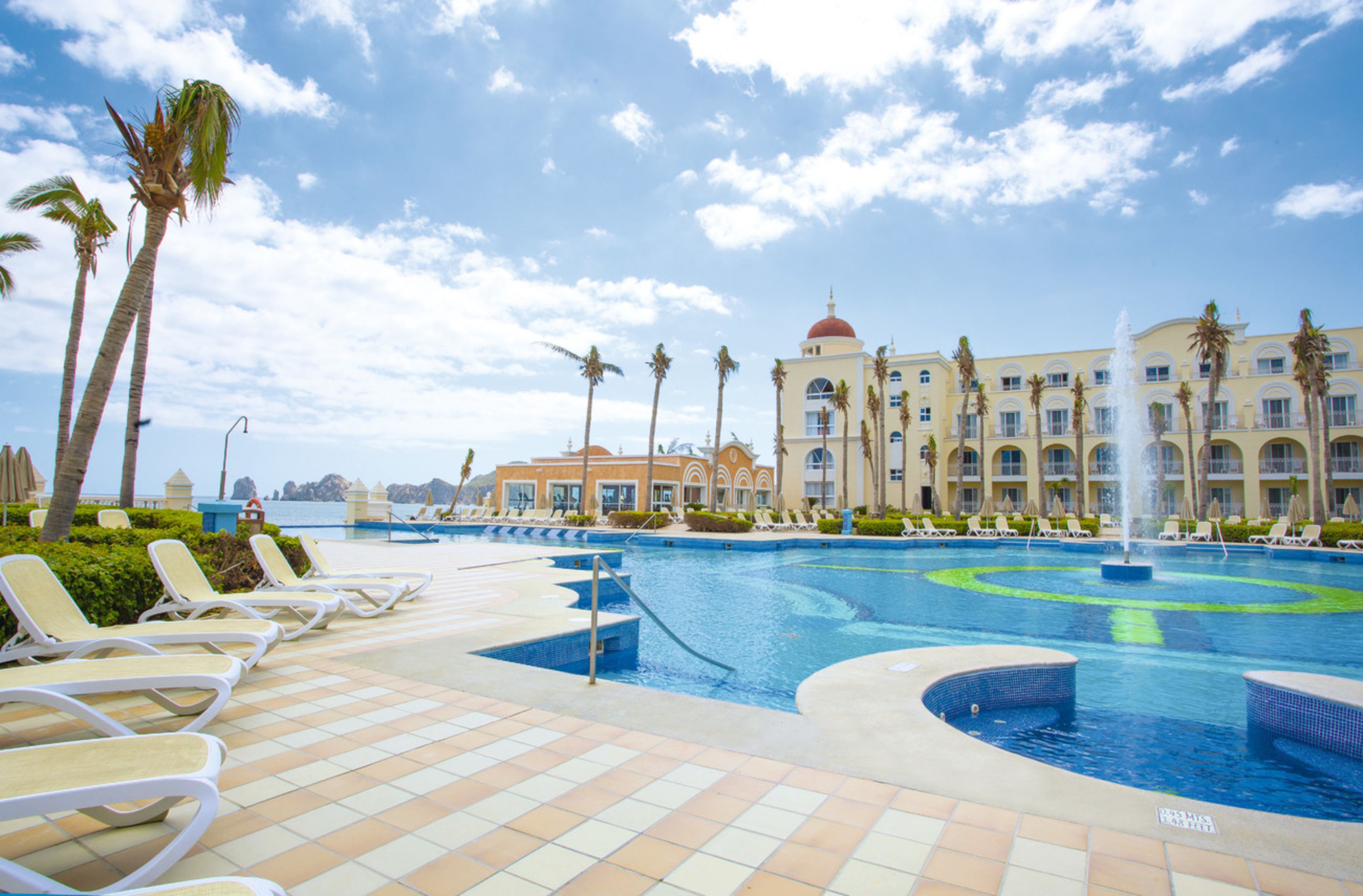 A hotel pool area with lounge chairs, palm trees, and a fountain.