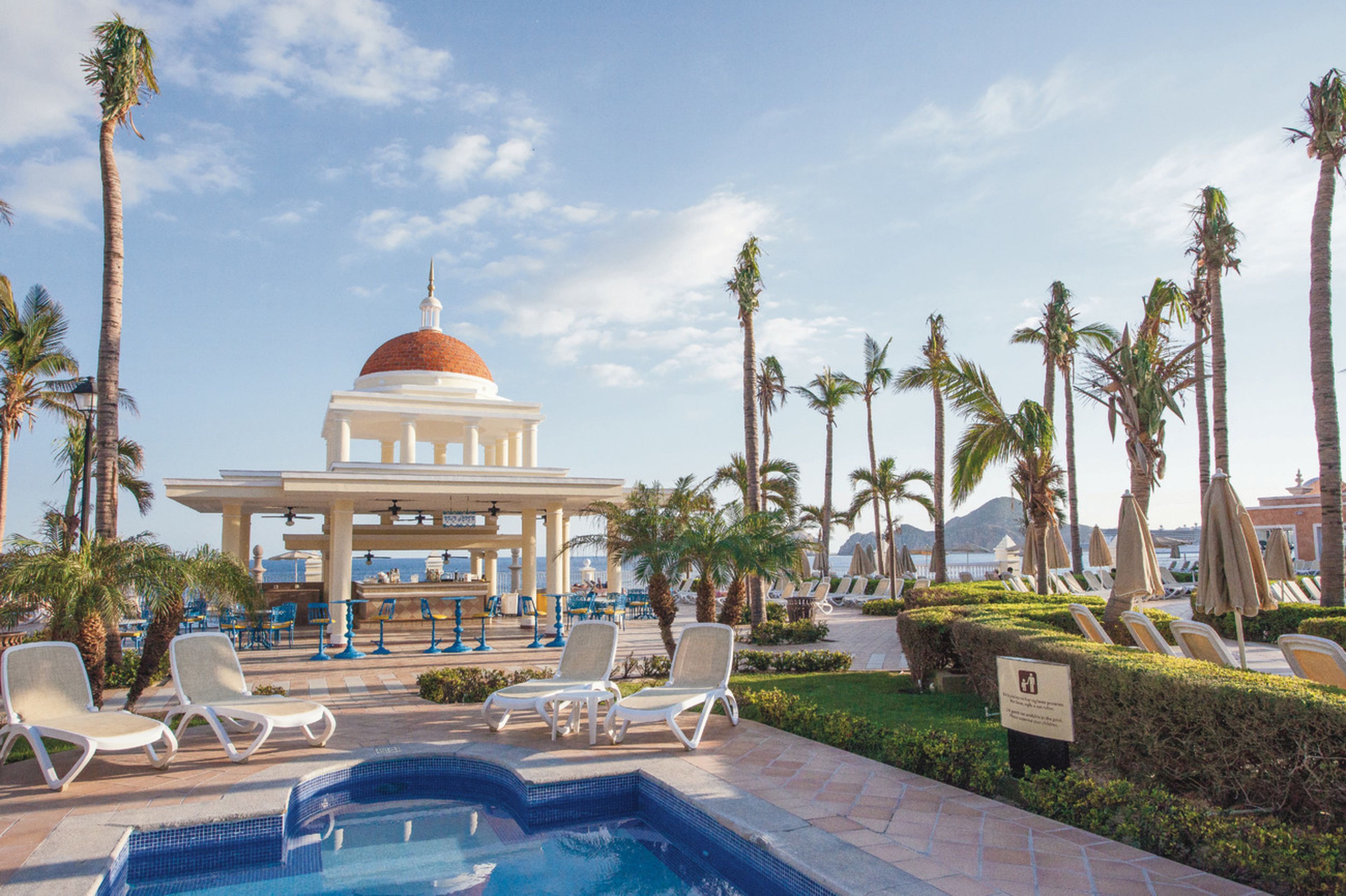 A pool area with lounge chairs and a gazebo with a dome.