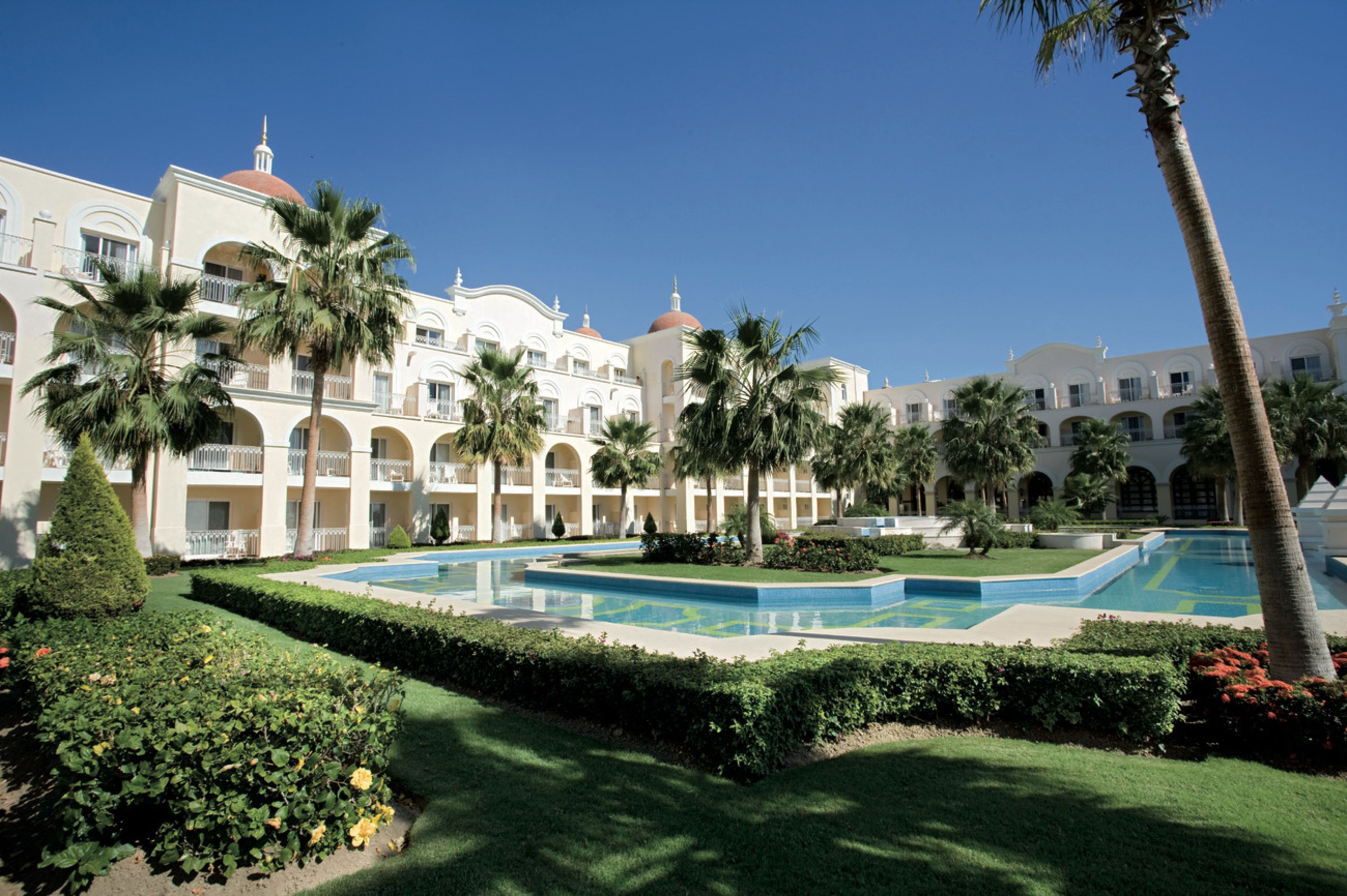 A hotel with multiple balconies, a swimming pool, and palm trees.