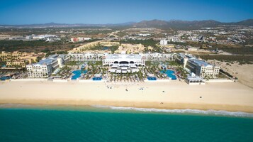 Vista aérea de un resort con varias edificaciones, una playa y una zona de piscina.