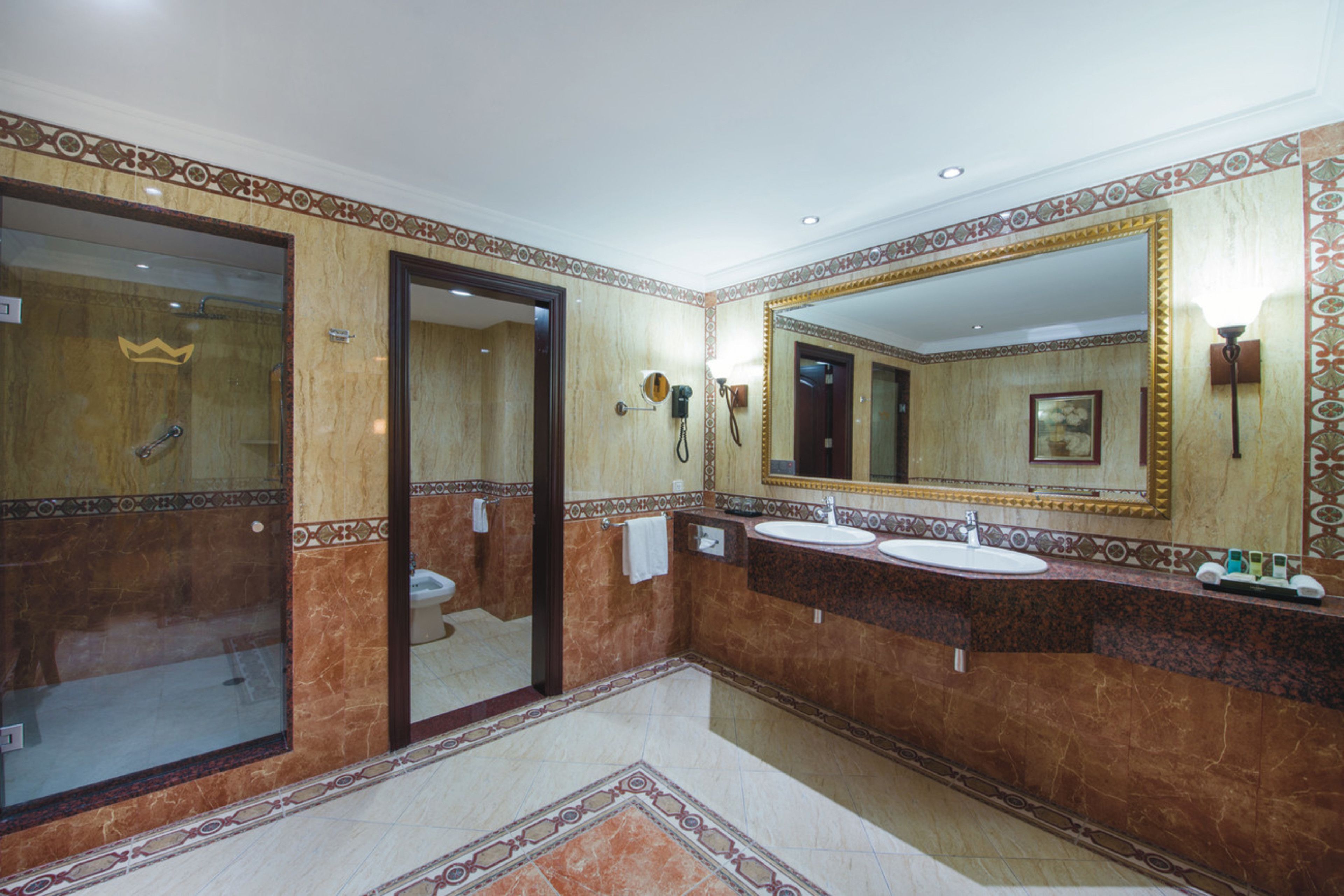 Un baño con tocador de mármol, dos lavamanos, un espejo grande y zona de ducha.