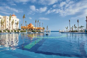 A resort pool with palm trees, a dome-roofed building, and a clear sky. - Hotel Riu Palace Cabo San Lucas - All Inclusive (Cabo San Lucas)