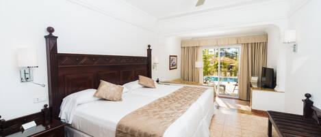 A hotel room with a large bed, a desk, a television, and a view of a pool.