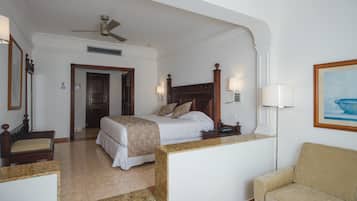 Una habitación de hotel con cama, escritorio, silla, sofá, ventilador de techo y un cuadro en la pared.