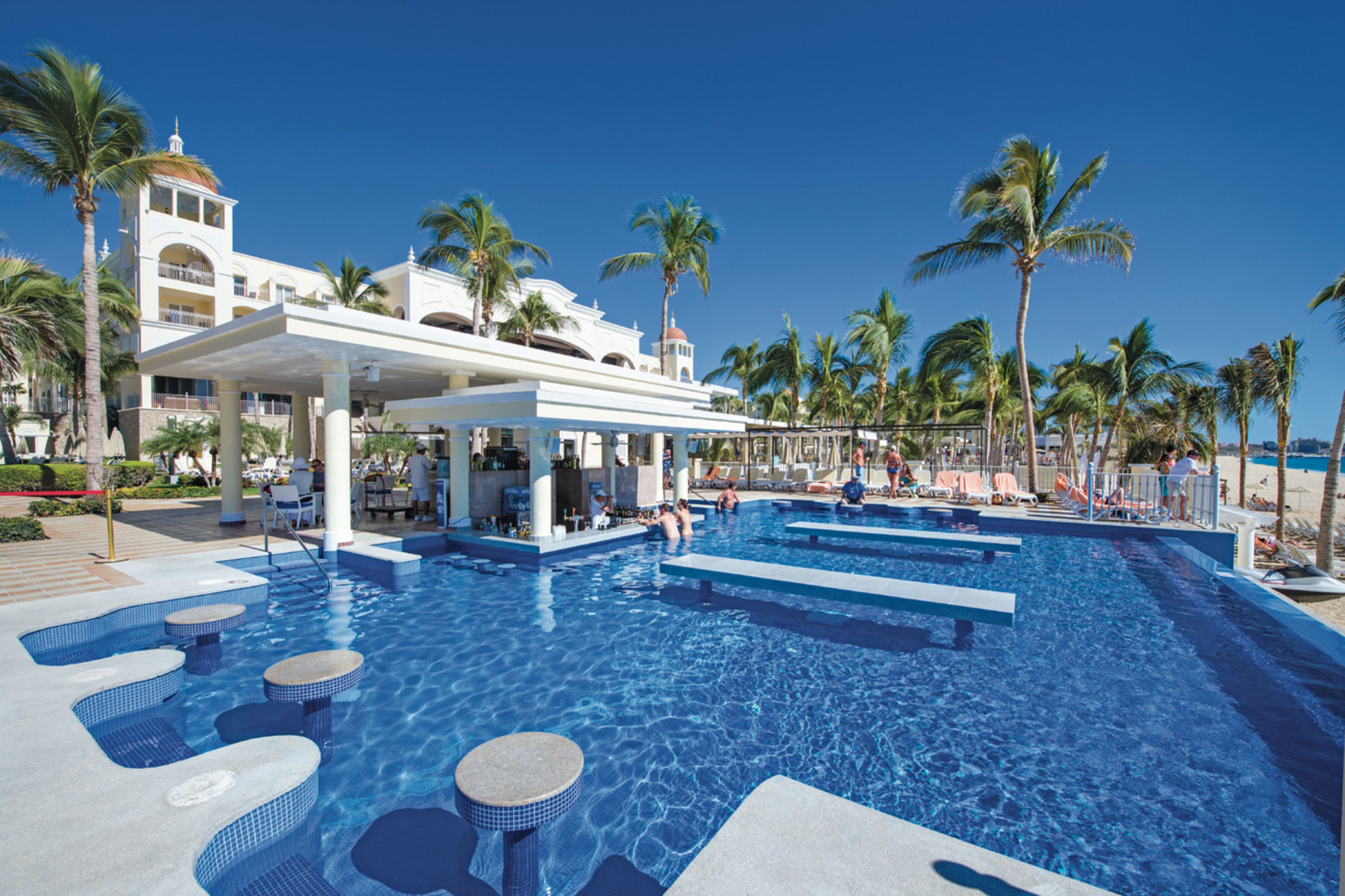 A resort pool area with multiple levels of seating and palm trees.
