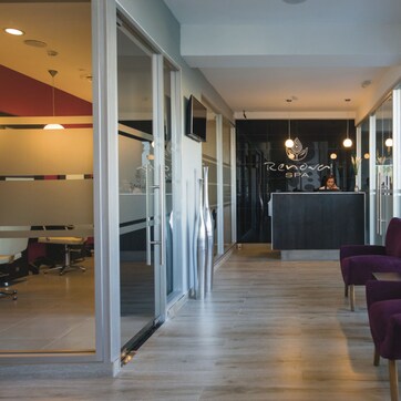 A modern spa reception area with a reception desk, purple chairs, and a glass wall.