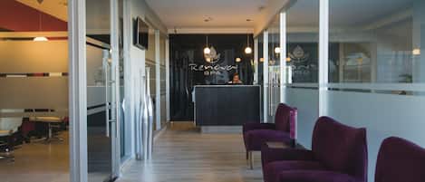 A modern spa reception area with a reception desk, purple chairs, and a glass wall.