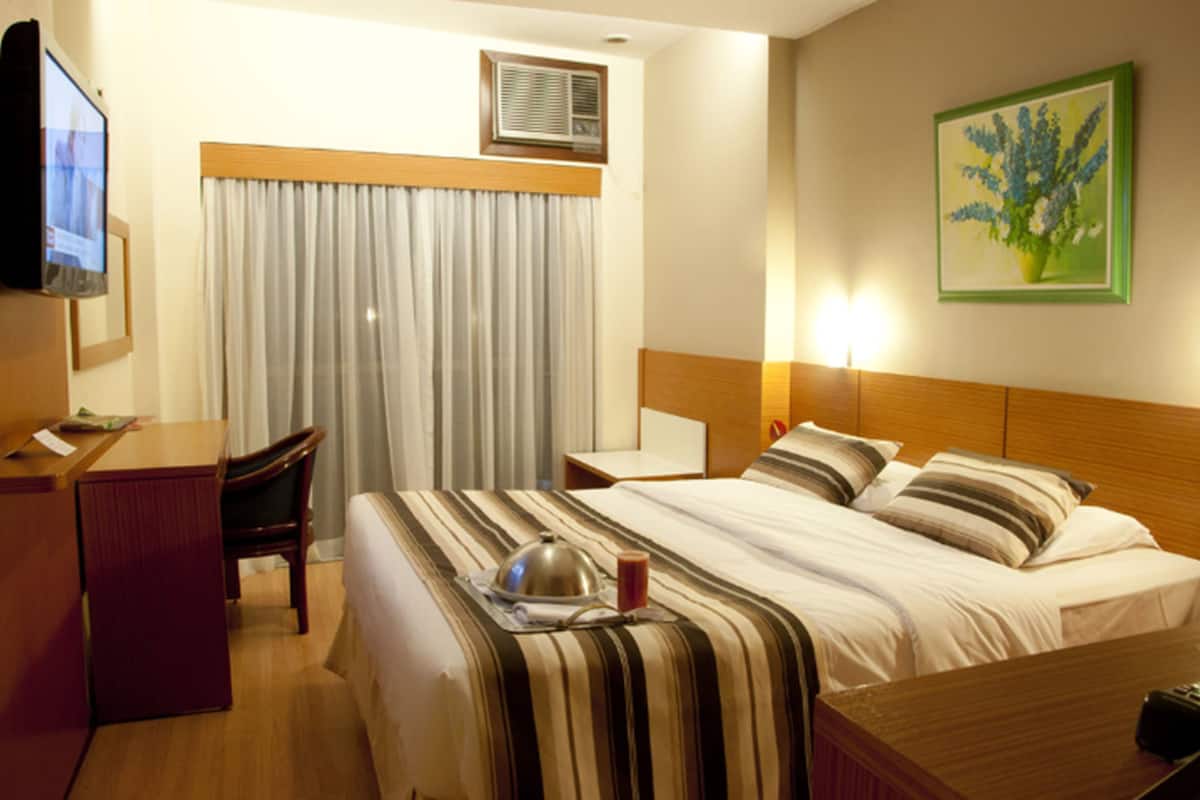 Une chambre d’hôtel avec un lit, un bureau, une chaise, une télévision et un tableau au mur.