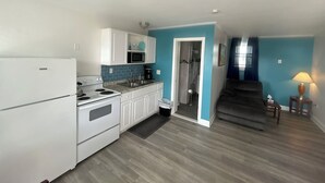 A compact kitchen with white appliances, a blue accent wall, and a staircase leading to a living area. - Thames Inn & Marina (Groton)