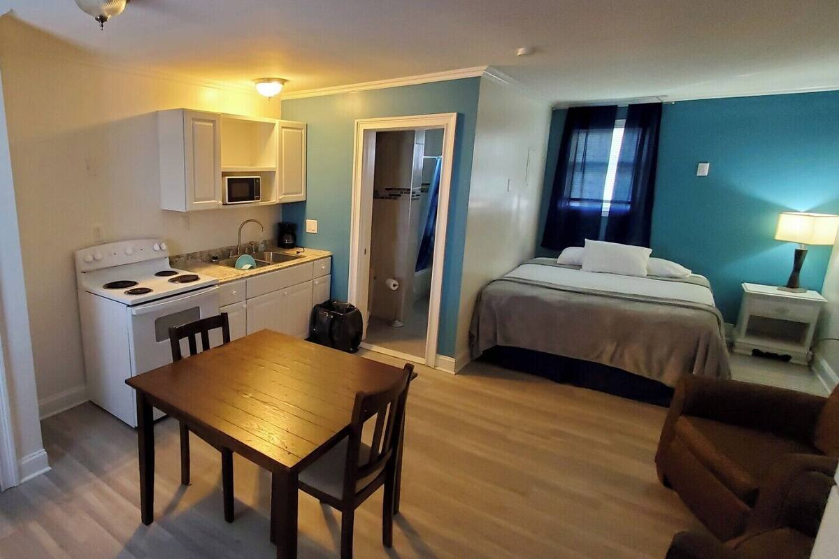 A compact hotel room with a kitchenette, a dining area, a bed, and a bathroom.