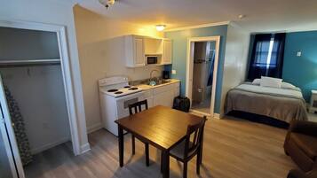 A compact hotel room with a kitchenette, a dining area, a bed, and a bathroom.