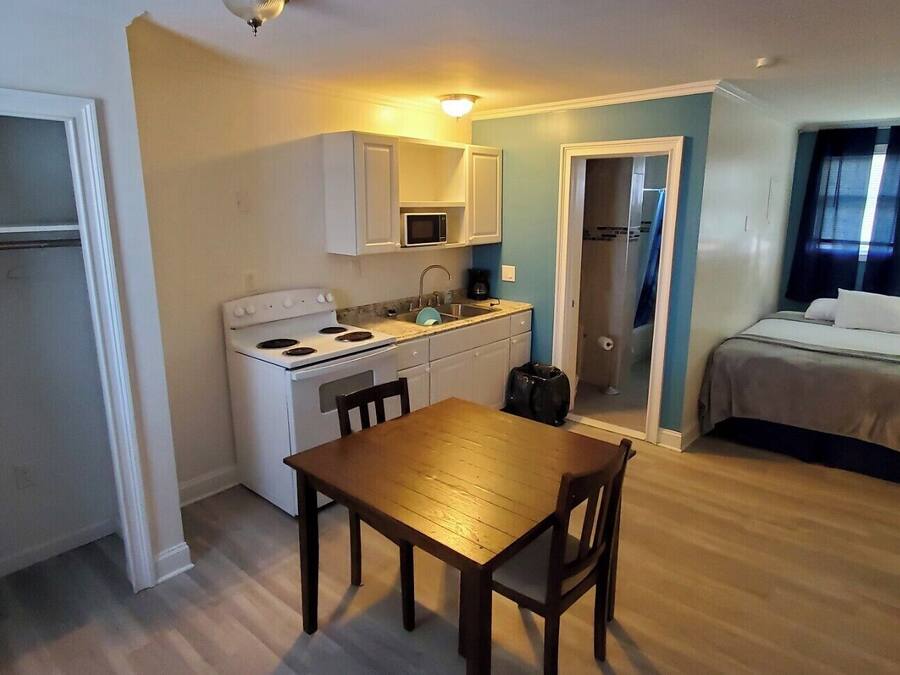 A compact hotel room with a kitchenette, a dining area, a bed, and a bathroom.